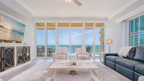 A spacious living room with a large window overlooking the ocean, a ceiling fan, and a modern fireplace. - Phoenix Gulf Towers 1005 4 Bedroom Condo (Orange Beach)