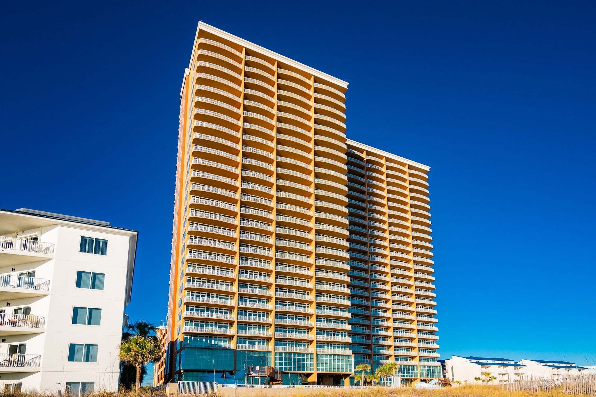 A high-rise hotel with multiple balconies, a modern architectural design, and a clear blue sky.