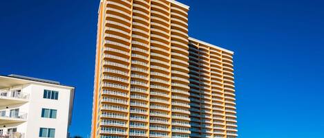 A high-rise hotel with multiple balconies, a modern architectural design, and a clear blue sky.