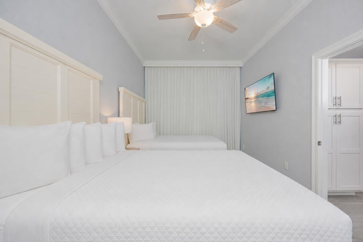 A bedroom with a large bed, a ceiling fan, a painting, and a door.