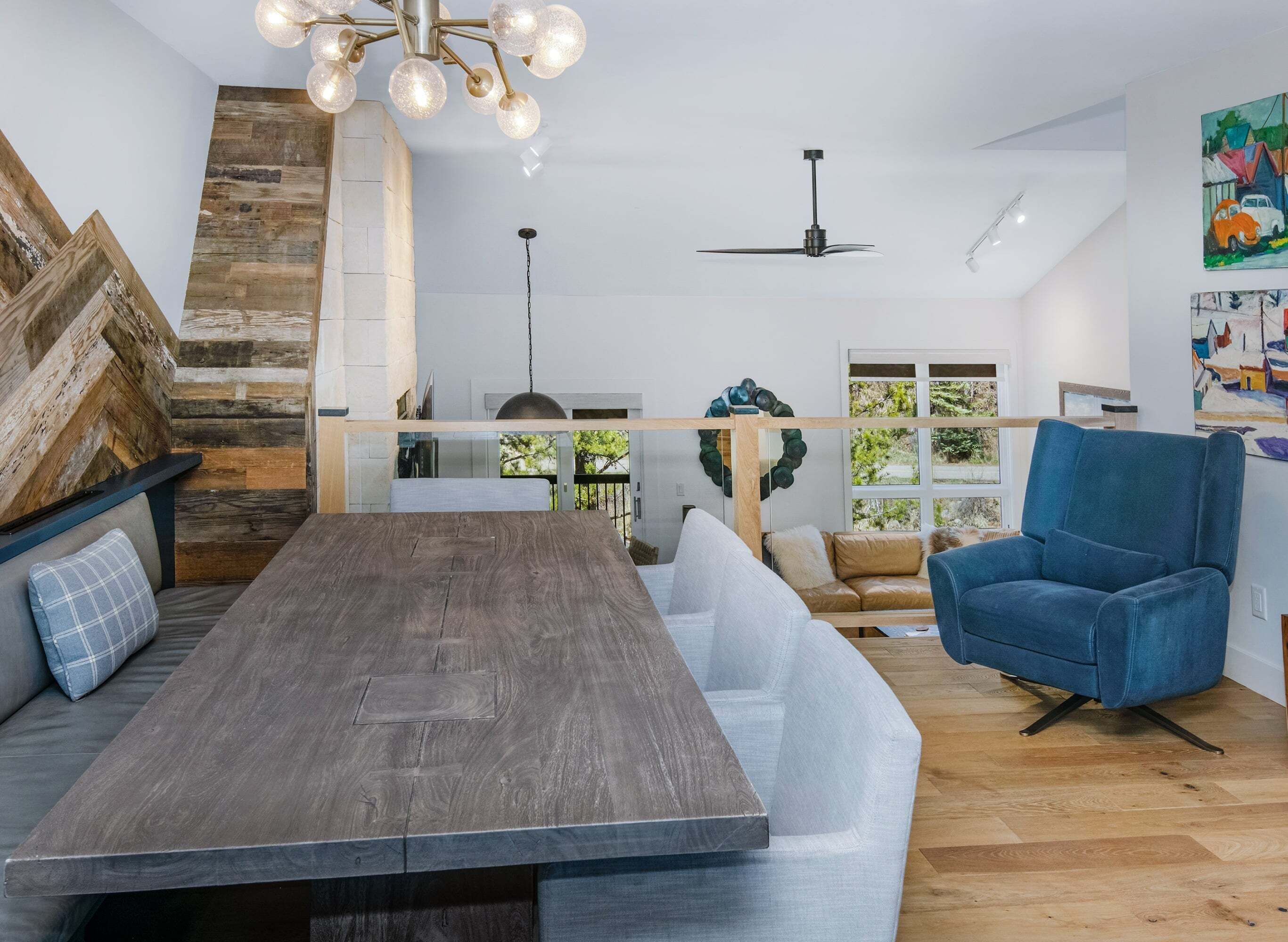 A modern kitchen with a wooden dining table, a blue armchair, and a staircase with exposed wooden beams.