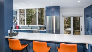 A modern kitchen with a large island, blue cabinets, and three orange bar stools. - Coldstream #18 3 Bedroom Townhouse (Vail)