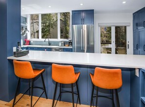 Une cuisine moderne dotée d’un grand îlot central, de meubles bleus et de trois tabourets de bar orange.