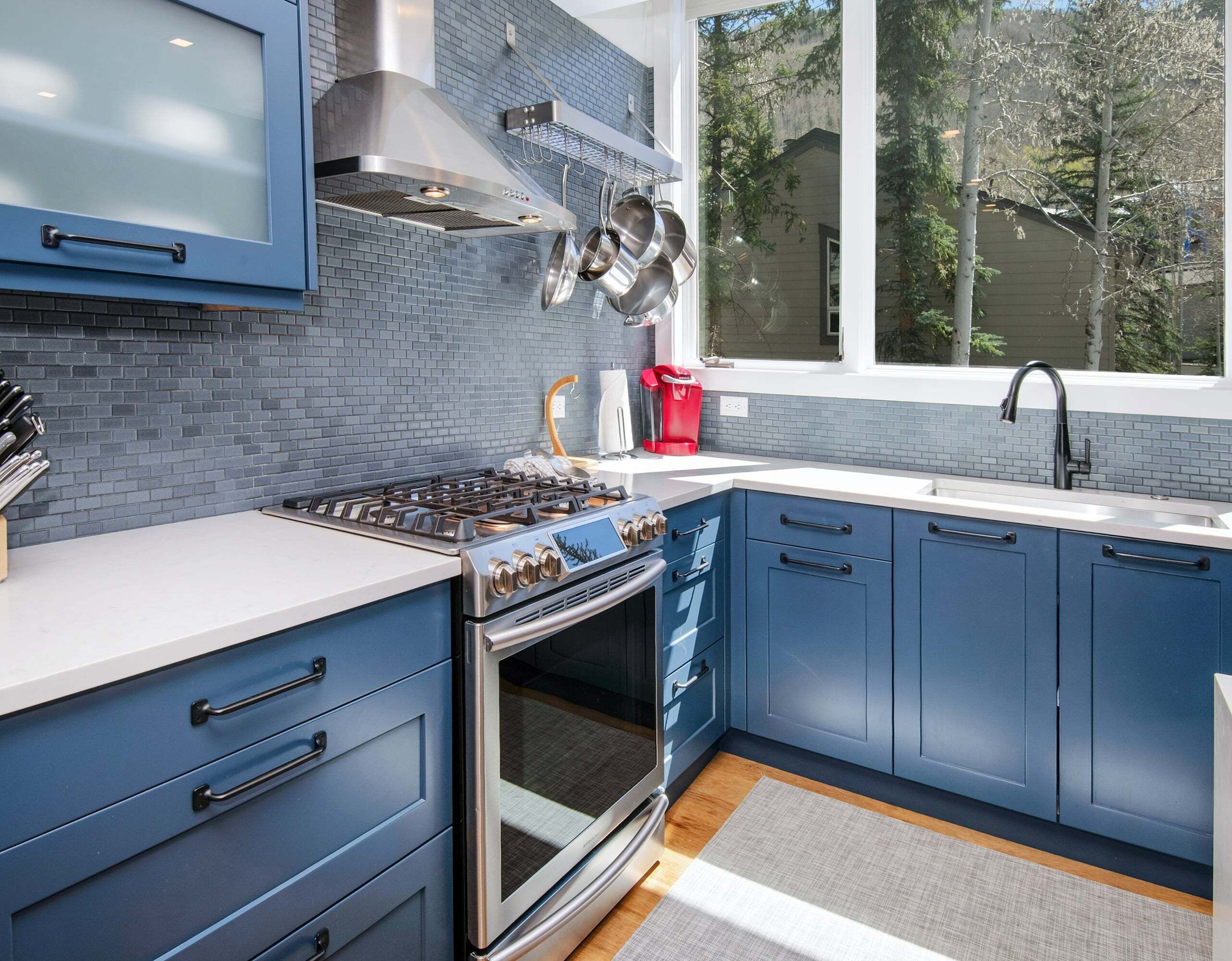 A modern kitchen with blue cabinets, a stainless steel range, and a window overlooking a residential area.