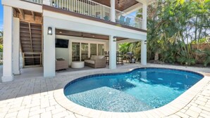 Una casa de dos pisos con piscina, mobiliario exterior y un patio cubierto.