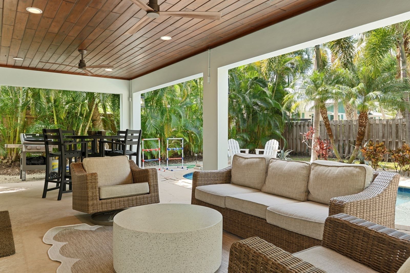 A covered outdoor area with a pool, wicker furniture, and a grill.