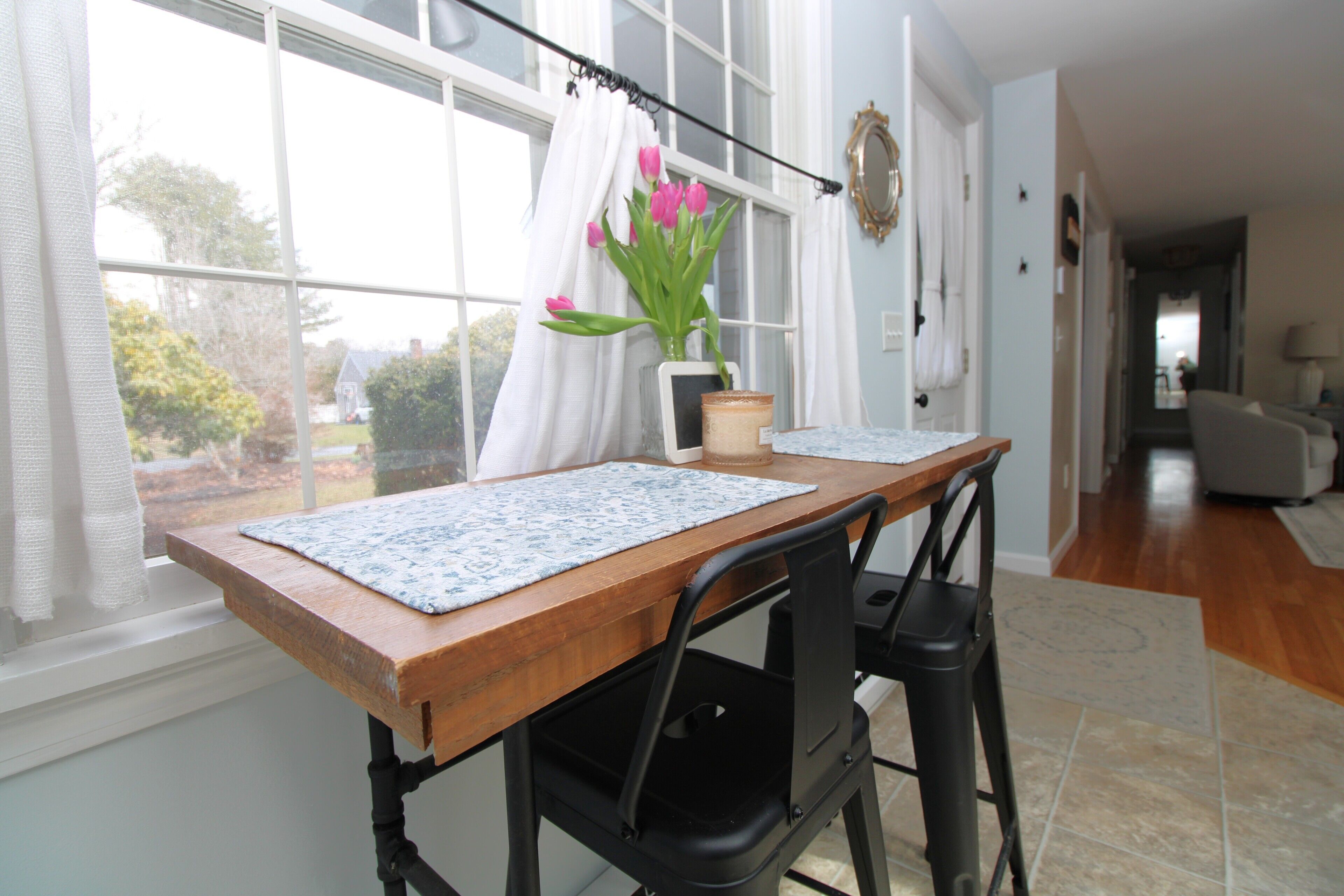 A dining table with a placemat, a potted plant, and a window with curtains.