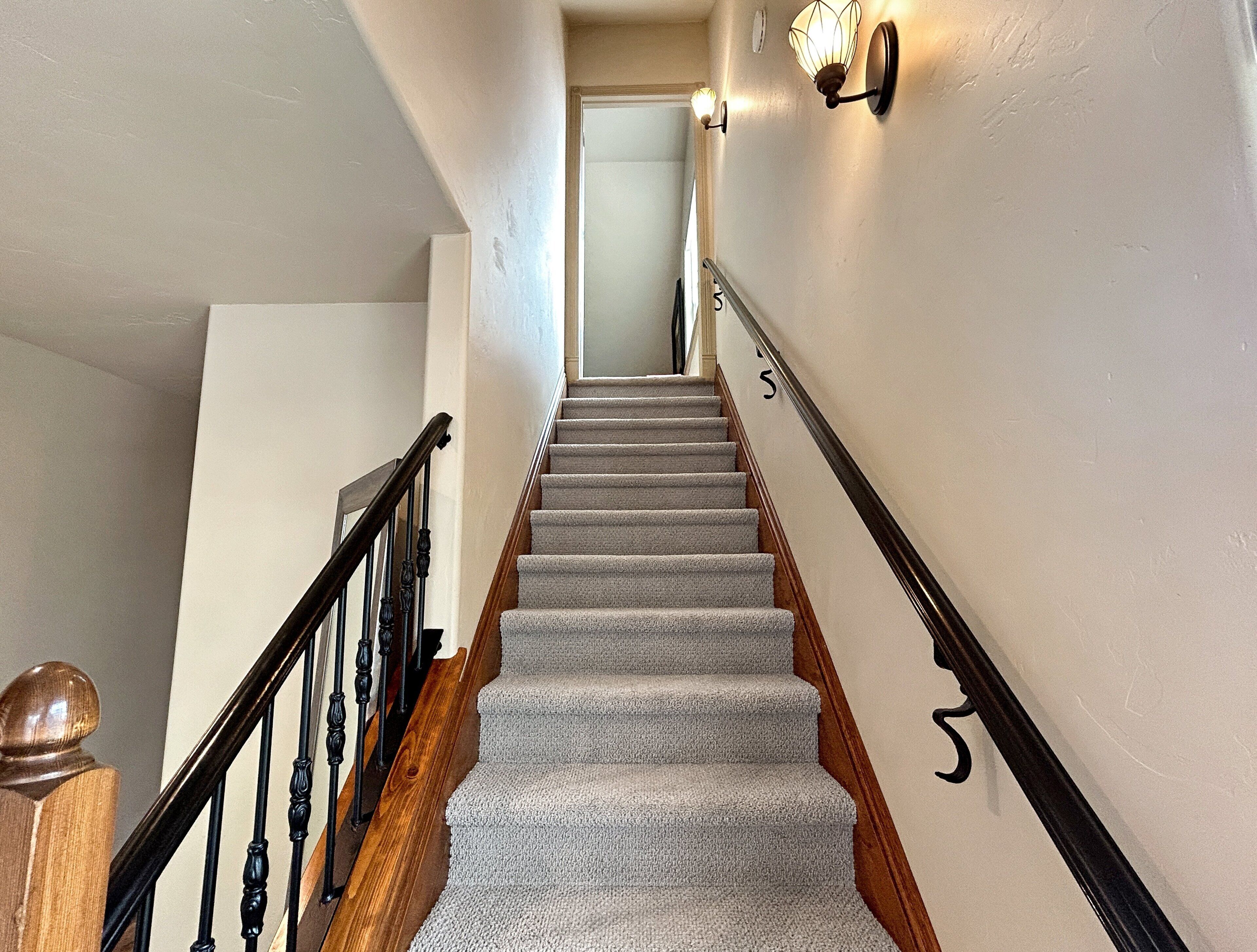 A staircase with carpeted steps, wooden handrails, and wall-mounted light fixtures.