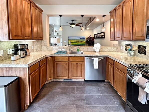 A kitchen with wooden cabinets, granite countertops, a stainless steel dishwasher, and a stove. - Victorian Chateau Retreat 3 Bedroom Townhouse (Grand Junction)