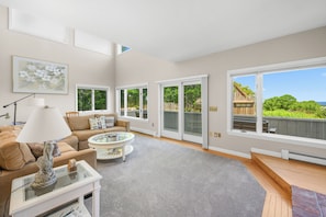 A spacious living room with a large window, a sofa, a coffee table, and a lamp.