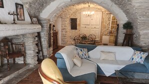 Ein Zimmer mit einer Steinwand, einer Kristalllüster, einem Bett mit blauer Bettwäsche, einem Holzstuhl und einem Fliesenboden.