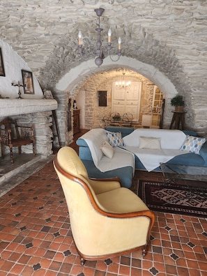 A room with a stone wall, a chandelier, a bed with blue bedding, a wooden chair, and a tiled floor. - CHARACTER VILLAGE HOUSE (Cabrières)