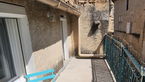Ein schmaler Außenbereich mit einem blauen Tisch und Stuhl, einer Steinmauer und einem Metallgeländer.