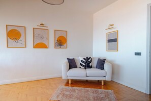 Ein weißes Sofa mit gemusterten Kissen, Holzboden und drei gerahmte Kunstwerke an der Wand.