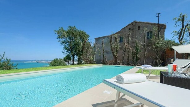 A swimming pool with a lounge area, a view of the sea, and a rustic building. - Villa Krizia - Ancona, beautifull villa with sea view pool (Ancona)