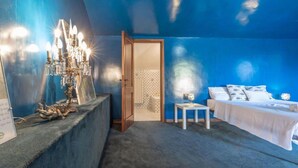 A room with a blue wall, a bed with white bedding, a small table, and a chandelier. - Villa Krizia - Ancona, beautifull villa with sea view pool (Ancona)