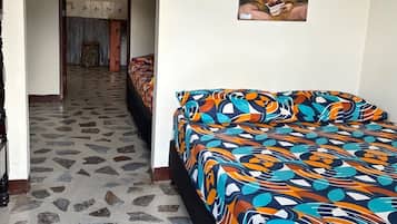 A room with a patterned floor, a bed with a colorful bedspread, a painting on the wall, and a hallway leading to another room.