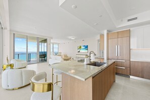 A modern kitchen with a large island, wooden cabinets, and a view of the ocean. - Luxury 2BR 2.5BA Amrit Condo with ocean view (Riviera Beach)