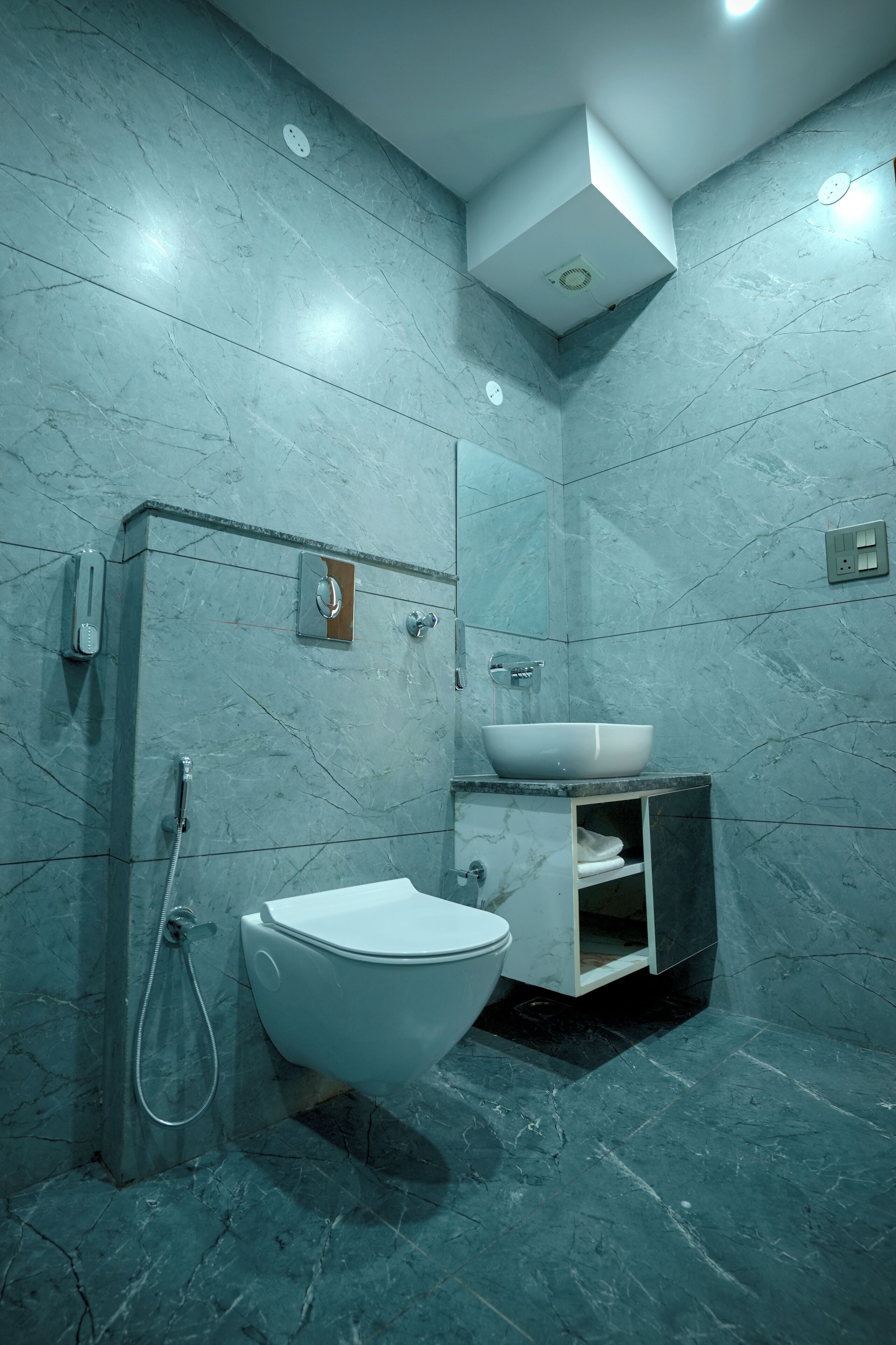 A bathroom with a toilet, bidet, and sink, all against a marble wall.