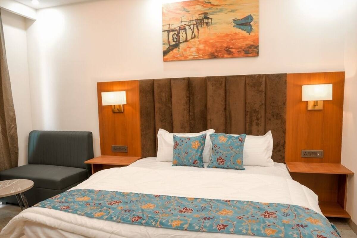 Une chambre d’hôtel avec un grand lit, deux tables de chevet, une tête de lit, un tableau au mur et un ventilateur de plafond.