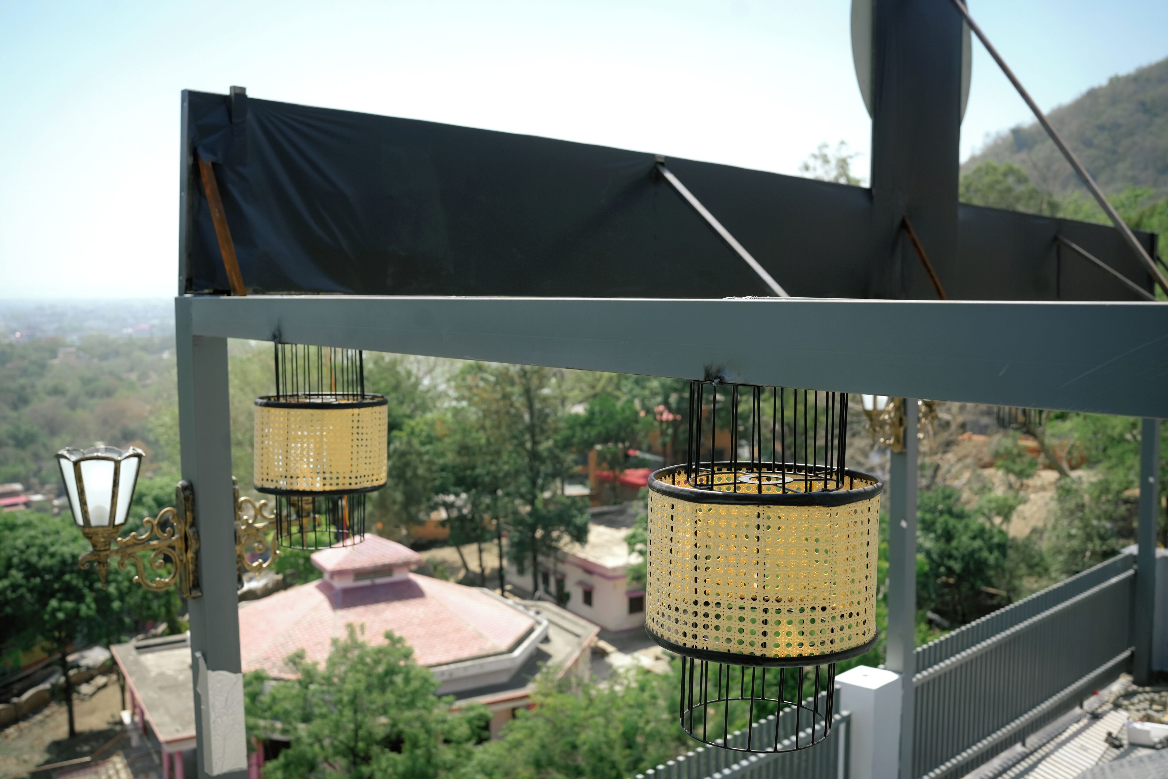 A balcony with hanging lamps and a view of buildings and trees.
