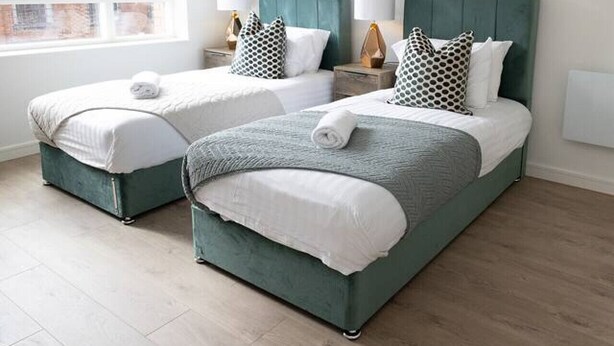 A modern bedroom with two beds, a city view, and a pendant light. - Cosy 2-Bedroom Flat with workspace (West Midlands)