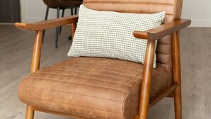 A brown leather chair with wooden armrests and a cushion, placed in a room with a wooden floor and a dining table in the background. - Cosy 2-Bedroom Flat with workspace (West Midlands)