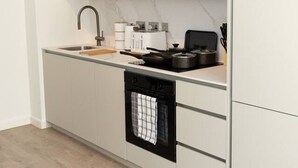 A modern kitchen with a wooden upper cabinet, a built-in oven, and a countertop with a kettle and pots. - Cosy 2-Bedroom Flat with workspace (West Midlands)