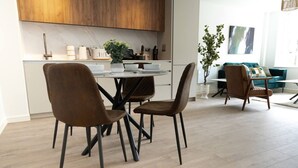 A modern kitchen with wooden cabinets, a dining table with four chairs, and a living area with a sofa and a plant. - Cosy 2-Bedroom Flat with workspace (West Midlands)