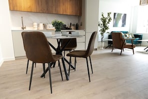 A modern kitchen with wooden cabinets, a dining table with four chairs, and a living area with a sofa and a plant. - Cosy 2-Bedroom Flat with workspace (West Midlands)
