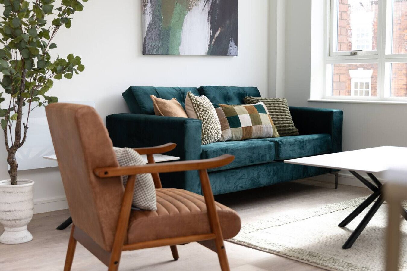 A living room with a teal sofa, a wooden armchair, a white coffee table, and a potted plant.