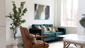 A living room with a teal sofa, a wooden chair, a potted plant, and a painting on the wall. - Cosy 2-Bedroom Flat with workspace (West Midlands)