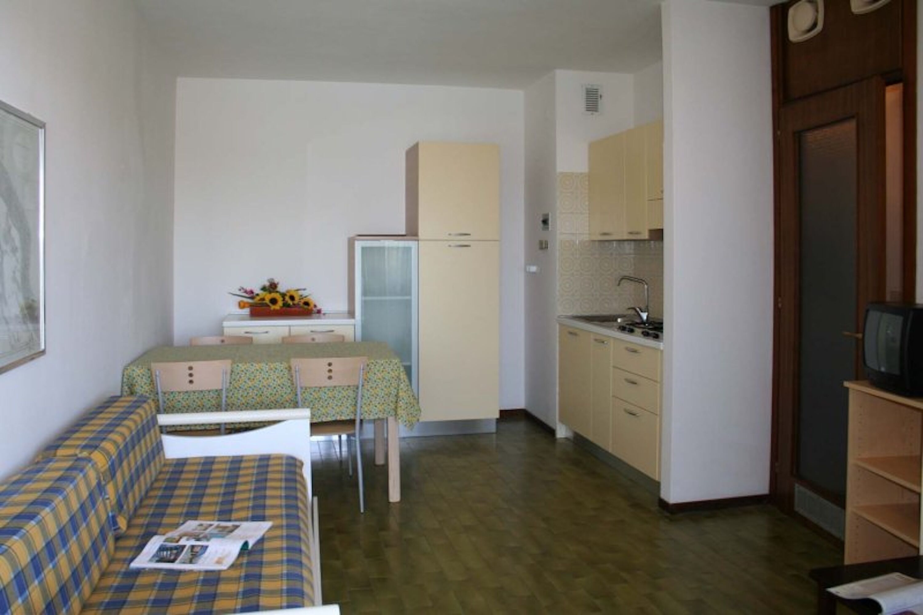 Una camera compatta con un letto, un piccolo tavolo da pranzo, angolo cottura con frigorifero e televisione.