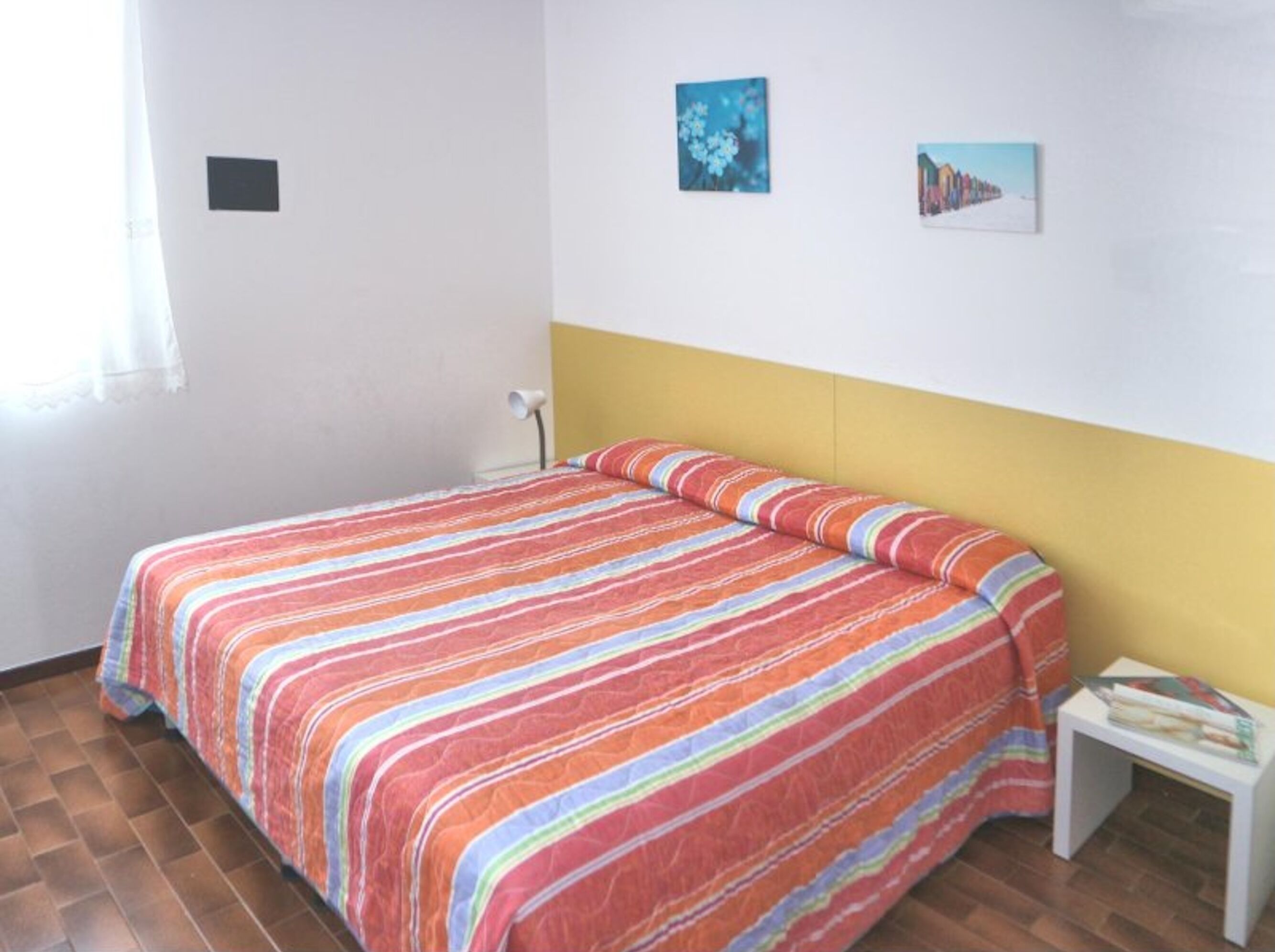 A bedroom with a striped bedspread, a small bedside table with a book, and two wall-mounted pictures.