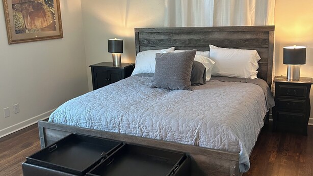 A bedroom with a bed, two bedside tables, a ceiling fan, a nightstand, a wooden floor, and a painting on the wall. - Marvelous 3-bedroom, newly renovated house with AC in charming Tyler (Tyler)