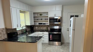 A kitchen with white cabinets, a black countertop, a microwave, an oven, and a refrigerator. - Marvelous 3-bedroom, newly renovated house with AC in charming Tyler (Tyler)