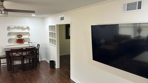 A living room with a large flat-screen TV, a dining area with a table and chairs, and a hallway leading to another room. - Marvelous 3-bedroom, newly renovated house with AC in charming Tyler (Tyler)