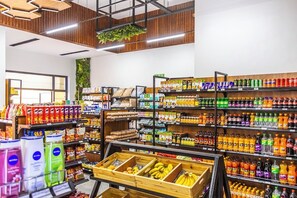Interior de um supermercado com prateleiras repletas de diversos produtos, uma exposição de bananas e um cesto de madeira.