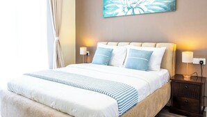 Ein ordentlich bezogenes Bett mit einer weiß-blauen Streifen-Decke, einem beigen Kopfteil und zwei Nachttischlampen.