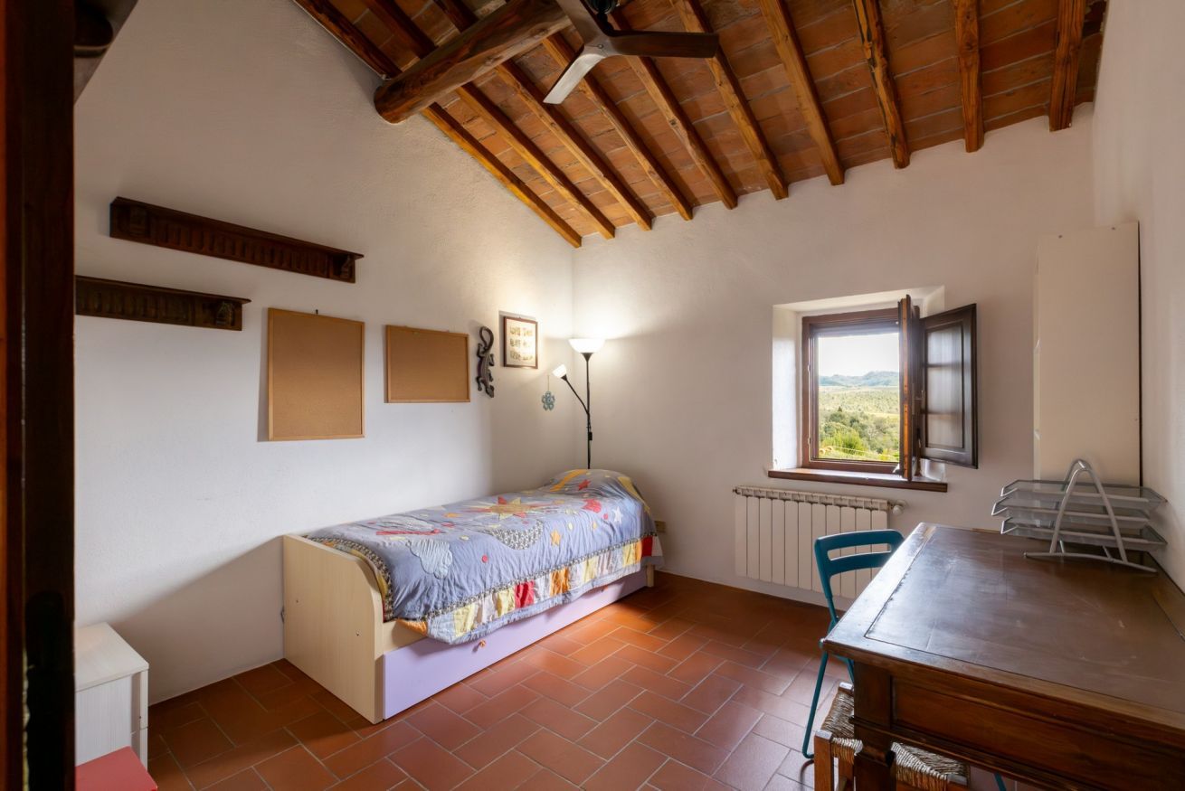 Una camera da letto con un letto, una scrivania, una sedia, una finestra e un termosifone.