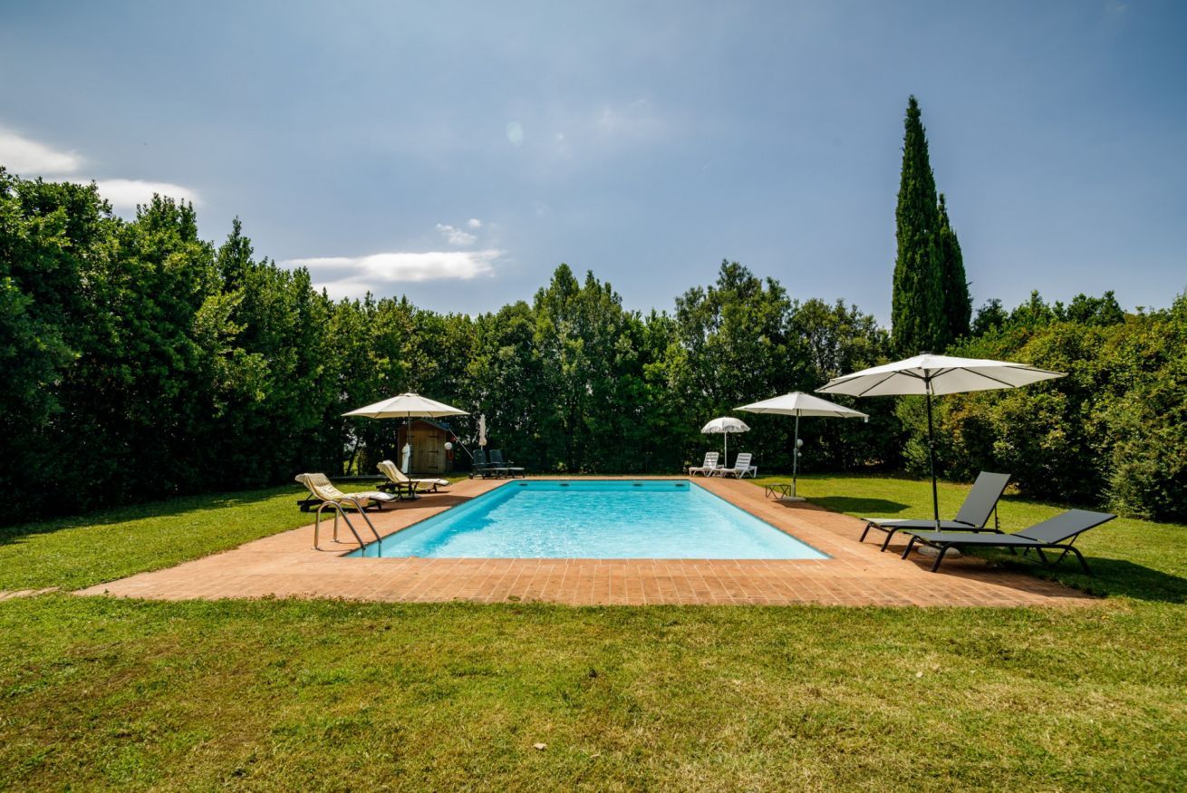 Ein rechteckiger Pool mit Liegestühlen und Sonnenschirmen, umgeben von einer Rasenfläche und Bäumen.