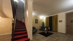Eine Treppe mit roten Stufen, ein dunkelrotes Sofa, ein kleiner Tisch und eine Pflanze in einem Wohnzimmer mit Holzboden.