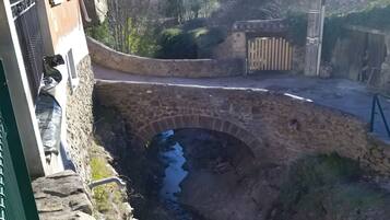 Un puente de piedra sobre un pequeño arroyo, un muro de piedra y un edificio con balcón.