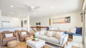 Una sala de estar moderna con sofá, sillones, una mesa de centro, ventilador de techo y una escalera.
