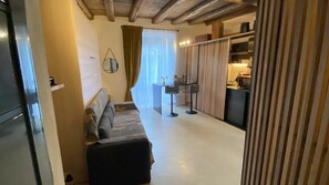 A compact living space with a sofa, a small table, and a kitchen area. - Suite Tagliamento Apartment with Wi-Fi and Air Conditioning (Caprarola)