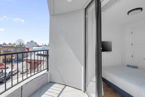 Ein Balkon mit Blick auf eine Stadtstraße, ein Bett mit Fernseher und eine Tür.