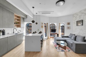 Eine moderne Küche mit Kochinsel, ein graues Sofa und ein Fernseher in einem gemütlichen Wohnbereich.
