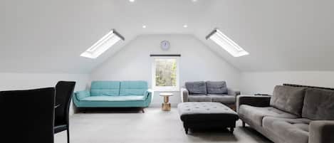 A loft-style room with a high ceiling, skylights, a sofa, a loveseat, a chair, and a small table.