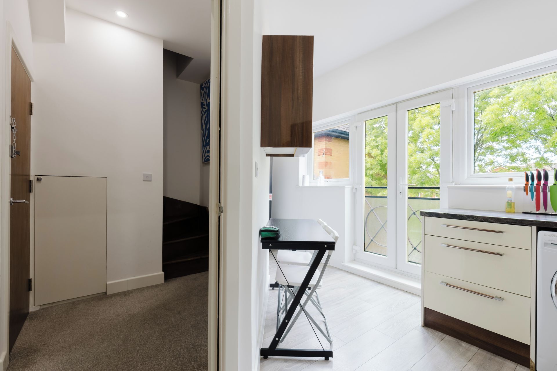 A modern kitchen with a built-in oven, a dining area with a table and chairs, and a view of greenery outside.