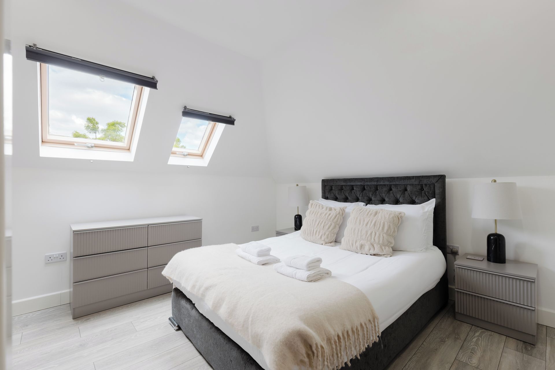 Un dormitorio moderno con una cama grande, dos mesitas de noche, un radiador y una ventana con vistas.
